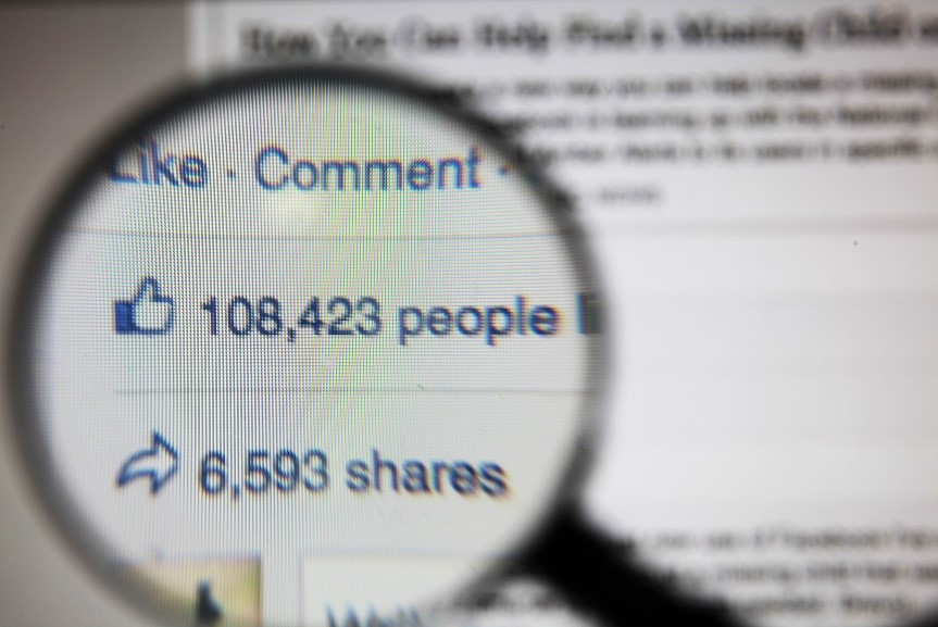 magnifying glass over Facebook data of likes and shares