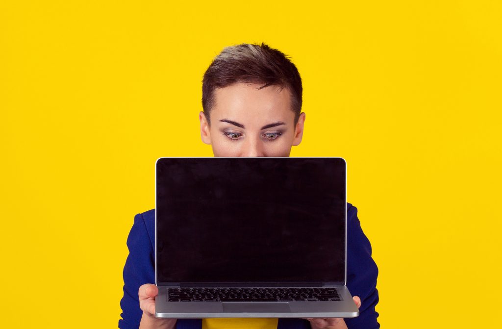 Closeup portrait happy smiling surprised businesswomen corporate employee, holding computer looking down at it isolated background yellow background. Positive stunned emotion on face